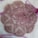 A circular crochet doily with intricate patterns and floral motifs lies on a soft, fluffy surface. The delicate lacework is highlighted against the background, and the doily features a symmetrical design with scalloped edges.