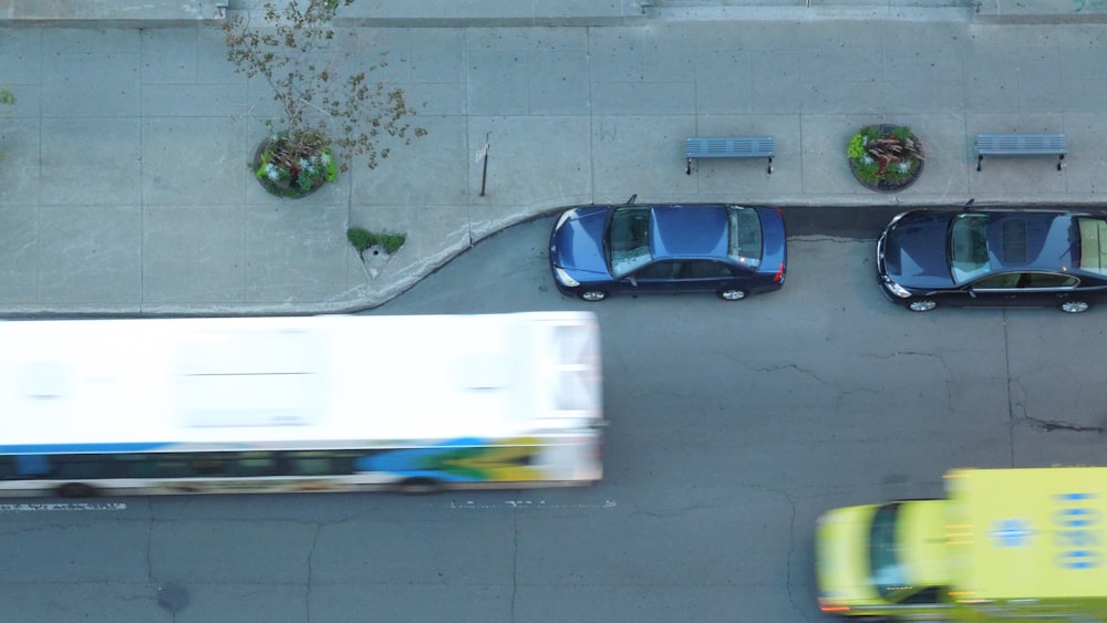 Fotografía aérea de dos vehículos azules estacionados cerca de un autobús en marcha y un camión amarillo-verde