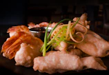 Golden crispy tempura shrimp served with a side of dipping sauce on a rustic wooden board.