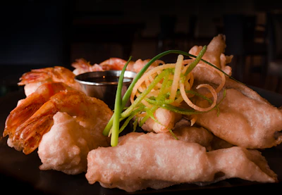 Golden crispy tempura shrimp served with a side of dipping sauce on a rustic wooden board.
