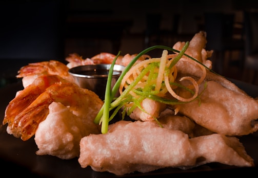 Close-up of crispy golden tempura shrimp served with dipping sauce on a rustic wooden table.