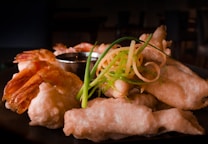 A beautifully arranged plate of deep-fried tempura shrimp and vegetables garnished with curly strips of green onion and a side of dipping sauce.