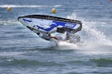 A person performing a stunt with a jet ski on water, partially submerged as the vehicle flips over while creating a splash.