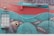 A vibrant and intricate mural decorates a red brick wall, featuring a large fish eye peering through ornate teal and turquoise patterns. These patterns flow across the wall, incorporating elements that suggest tentacles or waves. A large window and a red garage door are integrated into the artwork.