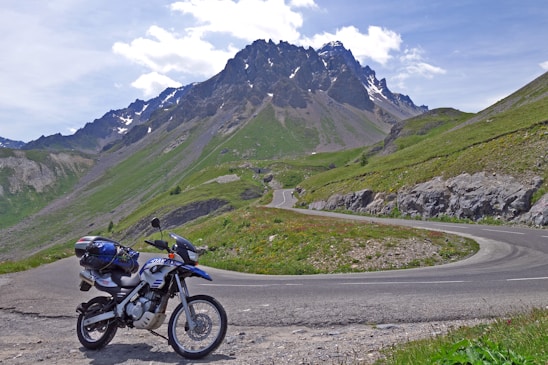 A scenic photo of a motorcycle parked on a winding mountain road with a panoramic view of European countryside.