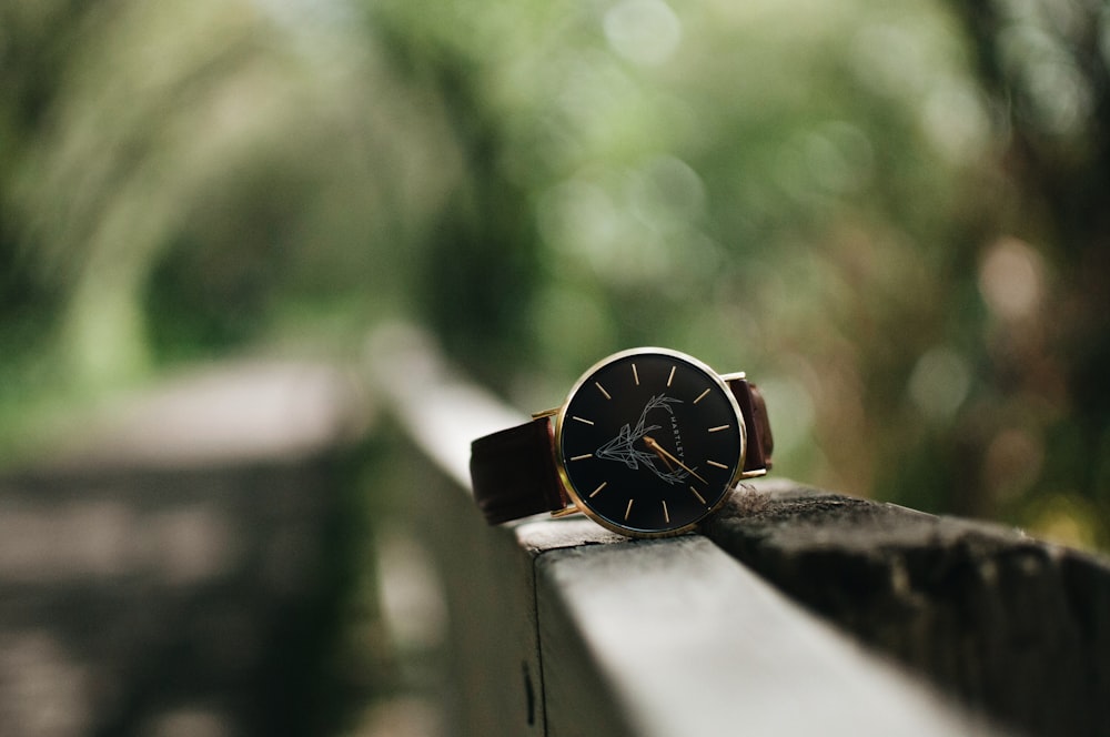 round silver-colored watch with black leather band on handrail