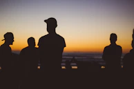 Silhouetted figures watching the empire fade beneath the ocean at dusk.