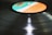 A close-up view of a vinyl record on a record player, with the label area colored in shades of turquoise, white, and orange. The grooves of the record reflect light, creating a shiny, smooth surface.