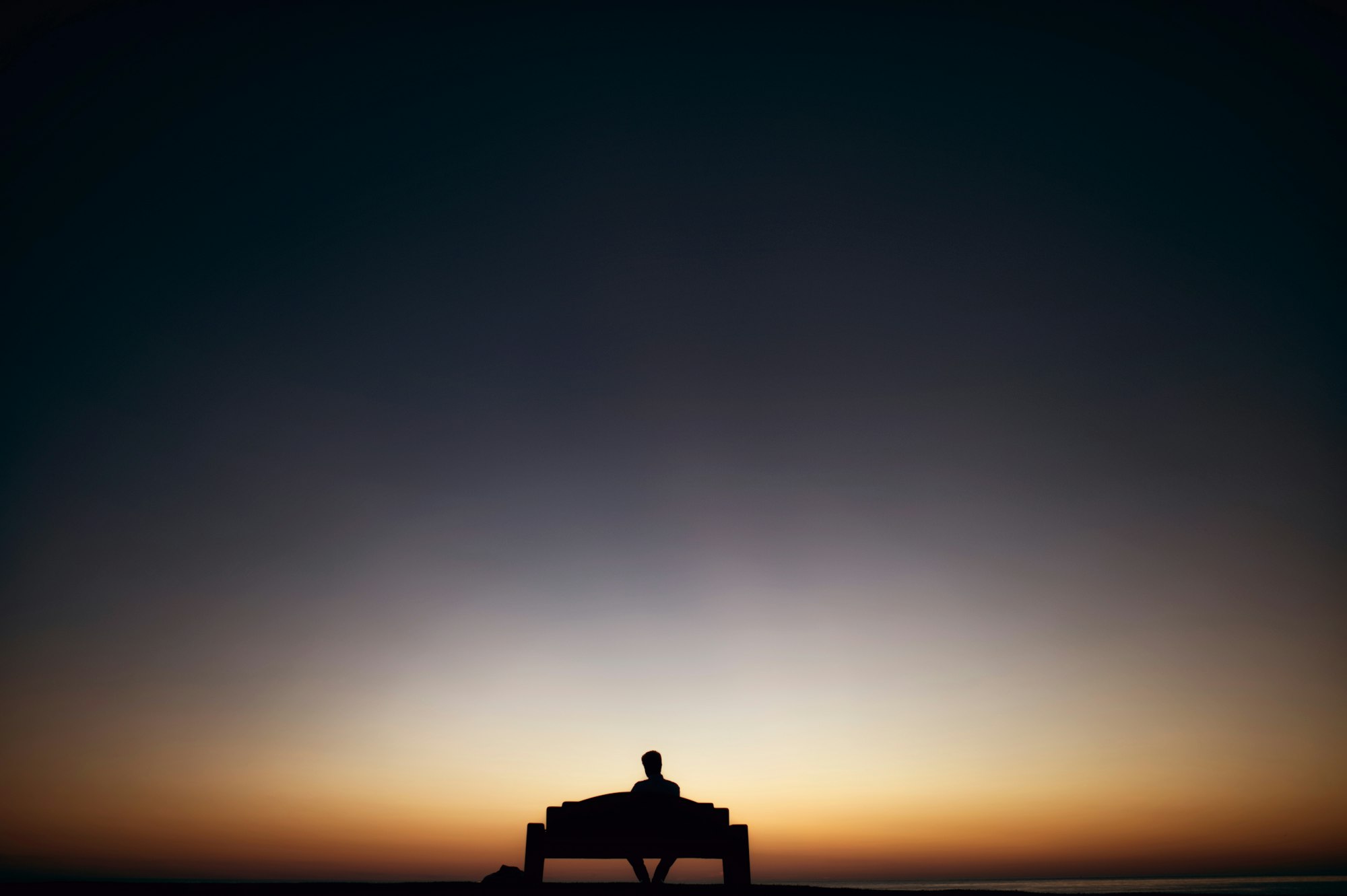 Man sitting on a bench during sunset.