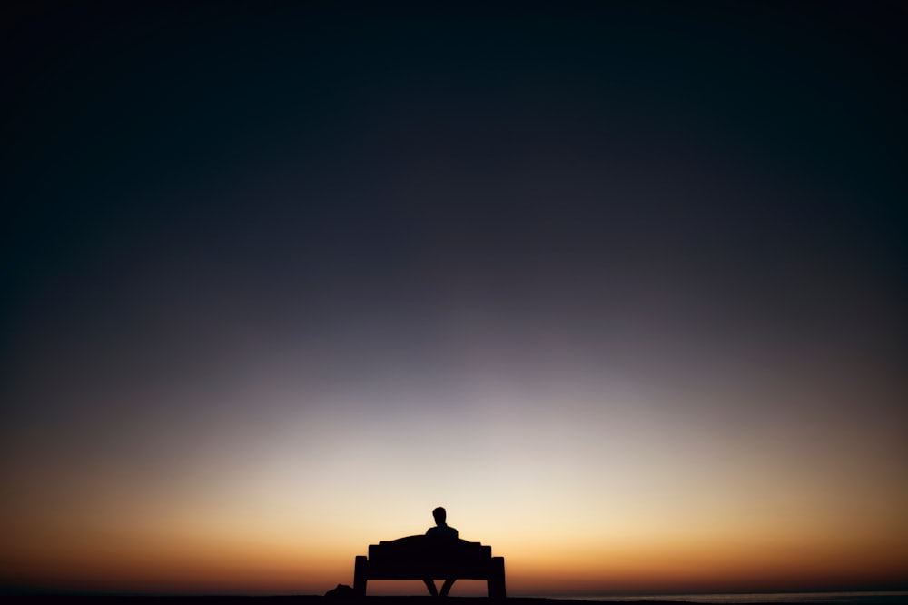 man sitting on bench facing sunset