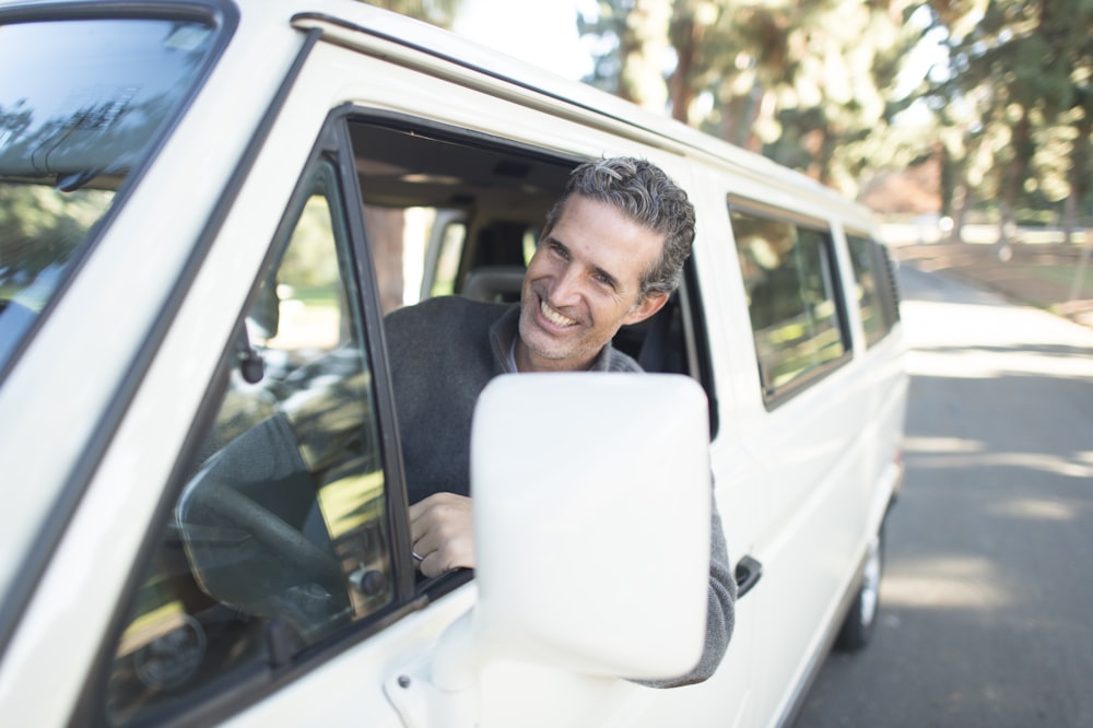 Mann im grauen Pullover lehnt sich an das Fenster des Lieferwagens