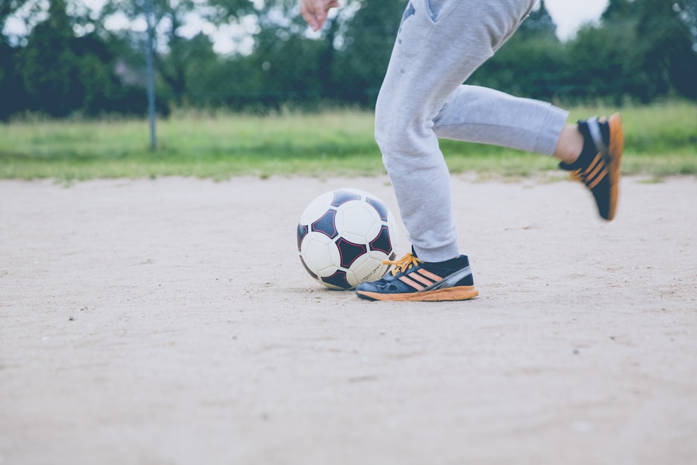 personne joue au ballon de football sur le sable blanc