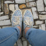 Close-up of pastel pink sneakers paired with light-wash denim jeans on a city sidewalk.