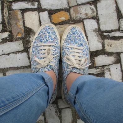 Close-up of pastel pink sneakers paired with light-wash denim jeans on a city sidewalk.