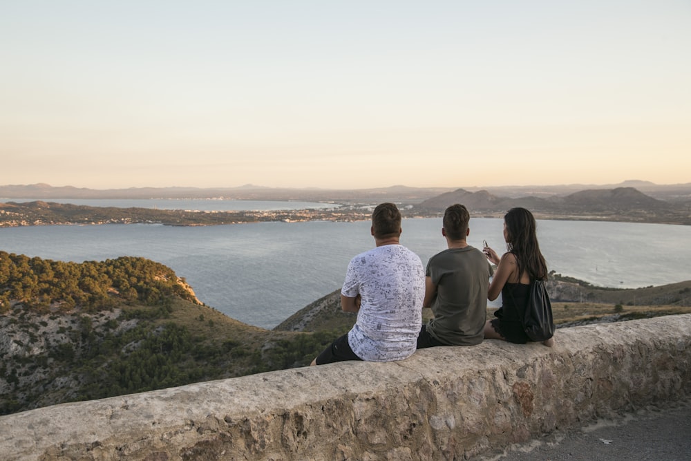 man and woman sitting on rock formation looking at the sea during daytime