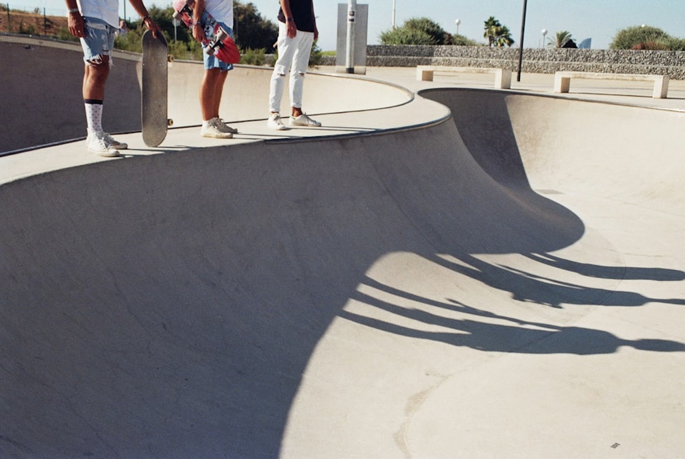 Drei Skater stehen tagsüber auf einer Skateboard-Betonrampe mit Schatten