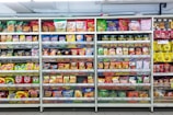A supermarket aisle filled with a variety of colorful packaged snacks arranged on metal shelving units. Different brands and flavors of chips and other snacks are prominently displayed, creating a vibrant and diverse display of products.