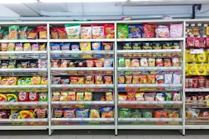 A supermarket aisle filled with a variety of colorful packaged snacks arranged on metal shelving units. Different brands and flavors of chips and other snacks are prominently displayed, creating a vibrant and diverse display of products.
