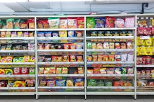 A supermarket aisle filled with a variety of colorful packaged snacks arranged on metal shelving units. Different brands and flavors of chips and other snacks are prominently displayed, creating a vibrant and diverse display of products.