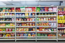 A supermarket aisle filled with a variety of colorful packaged snacks arranged on metal shelving units. Different brands and flavors of chips and other snacks are prominently displayed, creating a vibrant and diverse display of products.