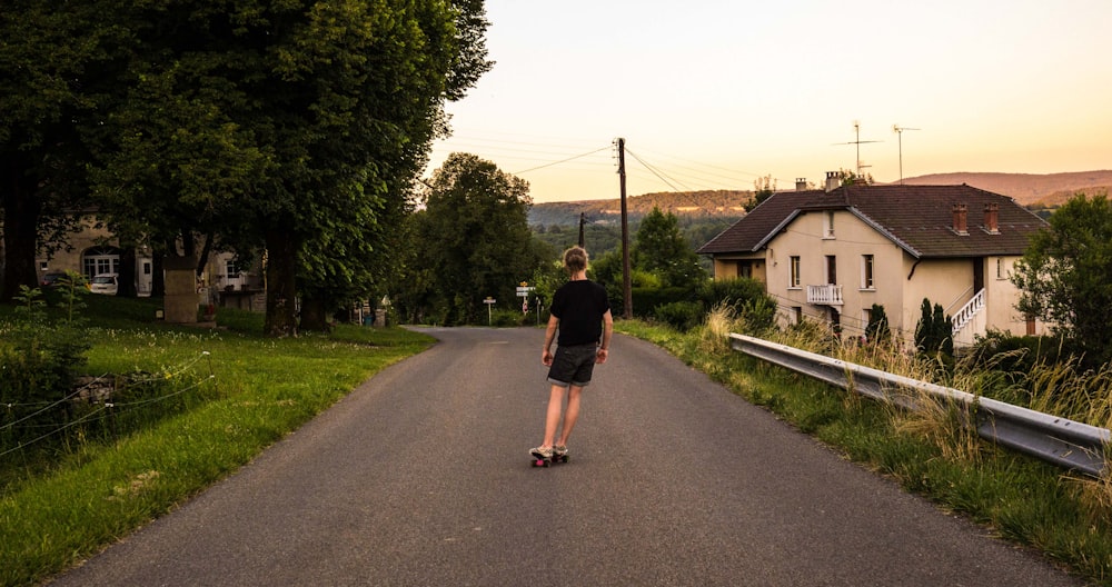 Donna in maglietta nera e pantaloncini neri che cammina sulla strada asfaltata grigia durante il giorno