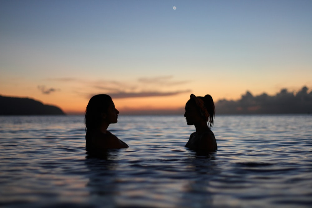 Silhouette of two women facing each other while standing in the waters of sunset Haleiwa beach