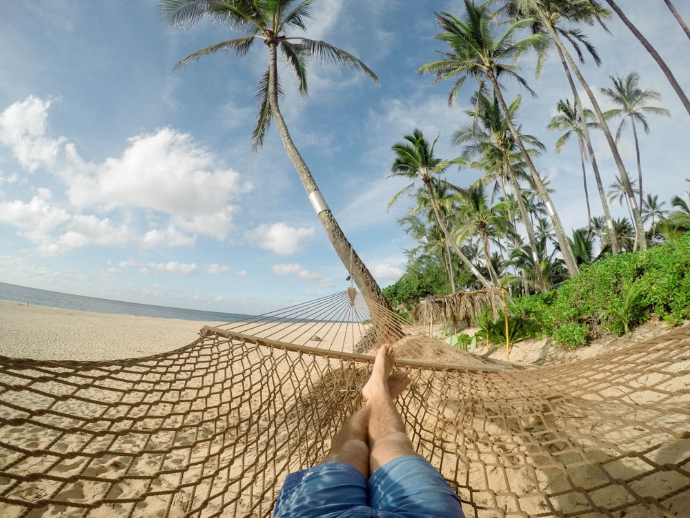 A person lying down in a hammock on the beach.