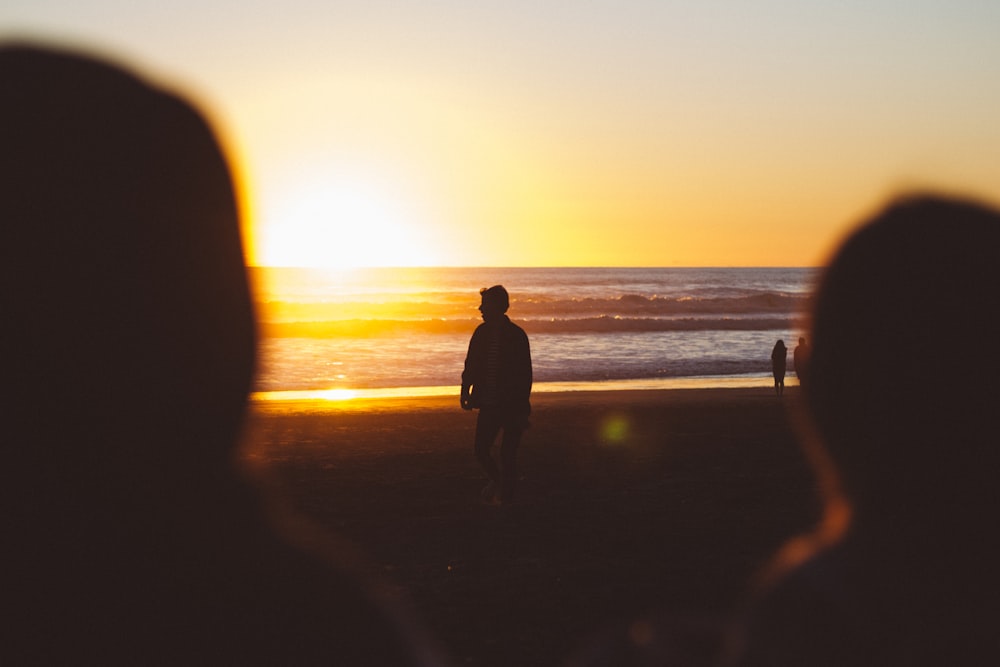 silhouette photo of man standing near seashore at sunset
