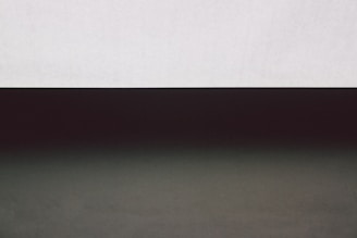 A minimalist composition with a stark contrast between two horizontal sections. The upper part is a light gray band, while the lower section is dark, creating a gradient effect.