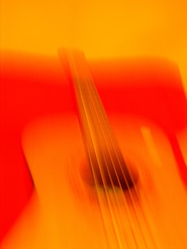 An abstract depiction of an acoustic guitar with motion blur, creating a warm, vibrant blend of orange and red hues.
