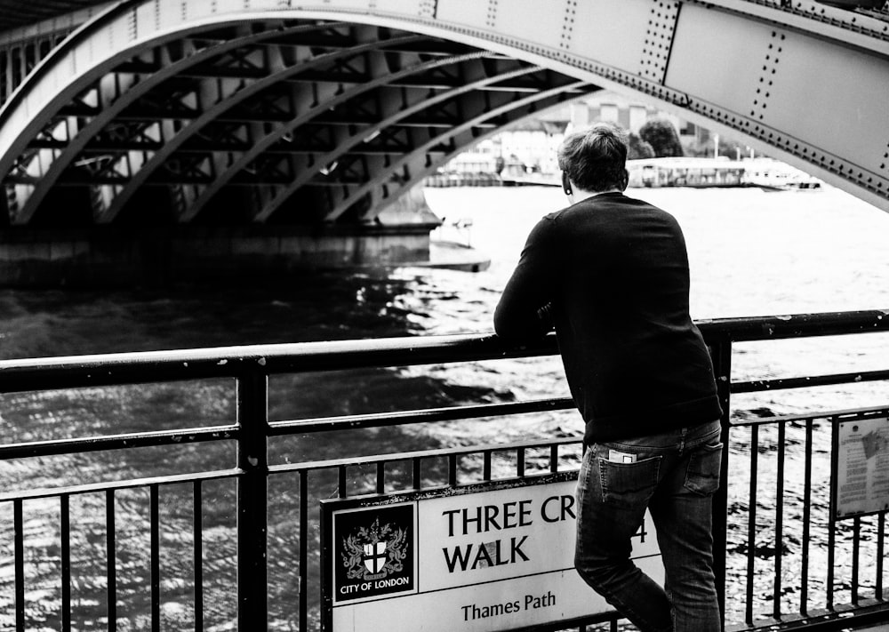 grayscale photo of man leaning on rails