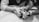 Hands of two individuals handling a vintage-style camera, focusing on the camera’s top control dials and lens. The image is in black and white, with a soft focus on the hands and camera, creating an intimate and nostalgic feel.