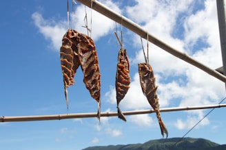 A close-up of sun-dried fish laid out on traditional wooden racks under a clear blue sky.