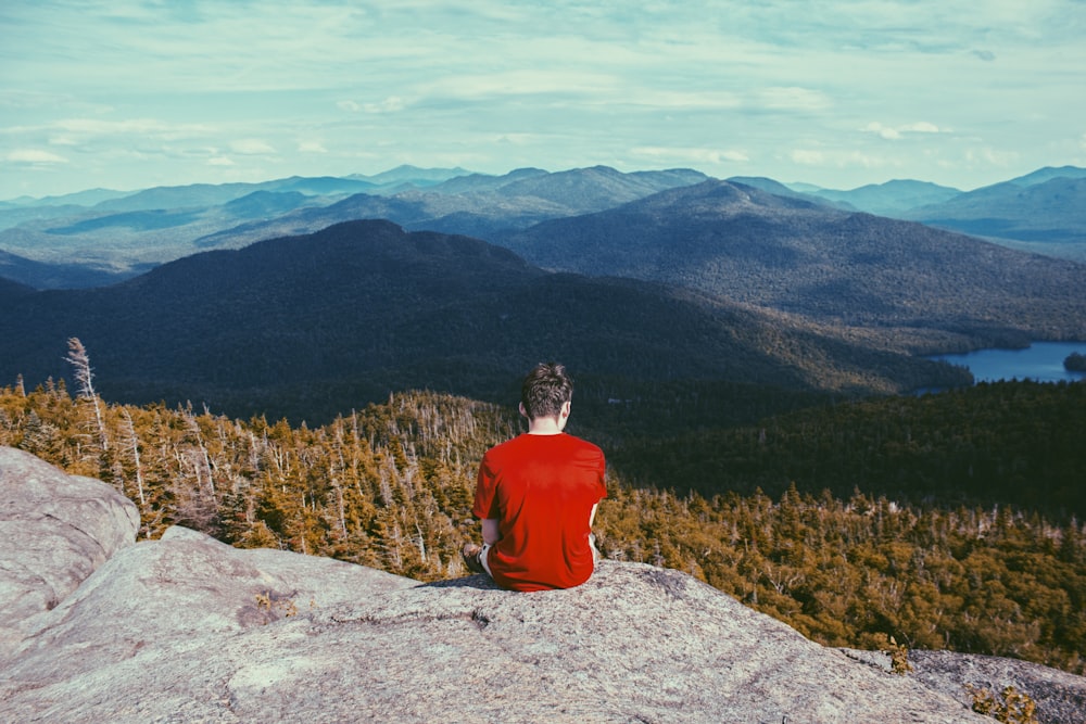 uomo che si siede sulla formazione rocciosa grigia che guarda i pini durante il giorno