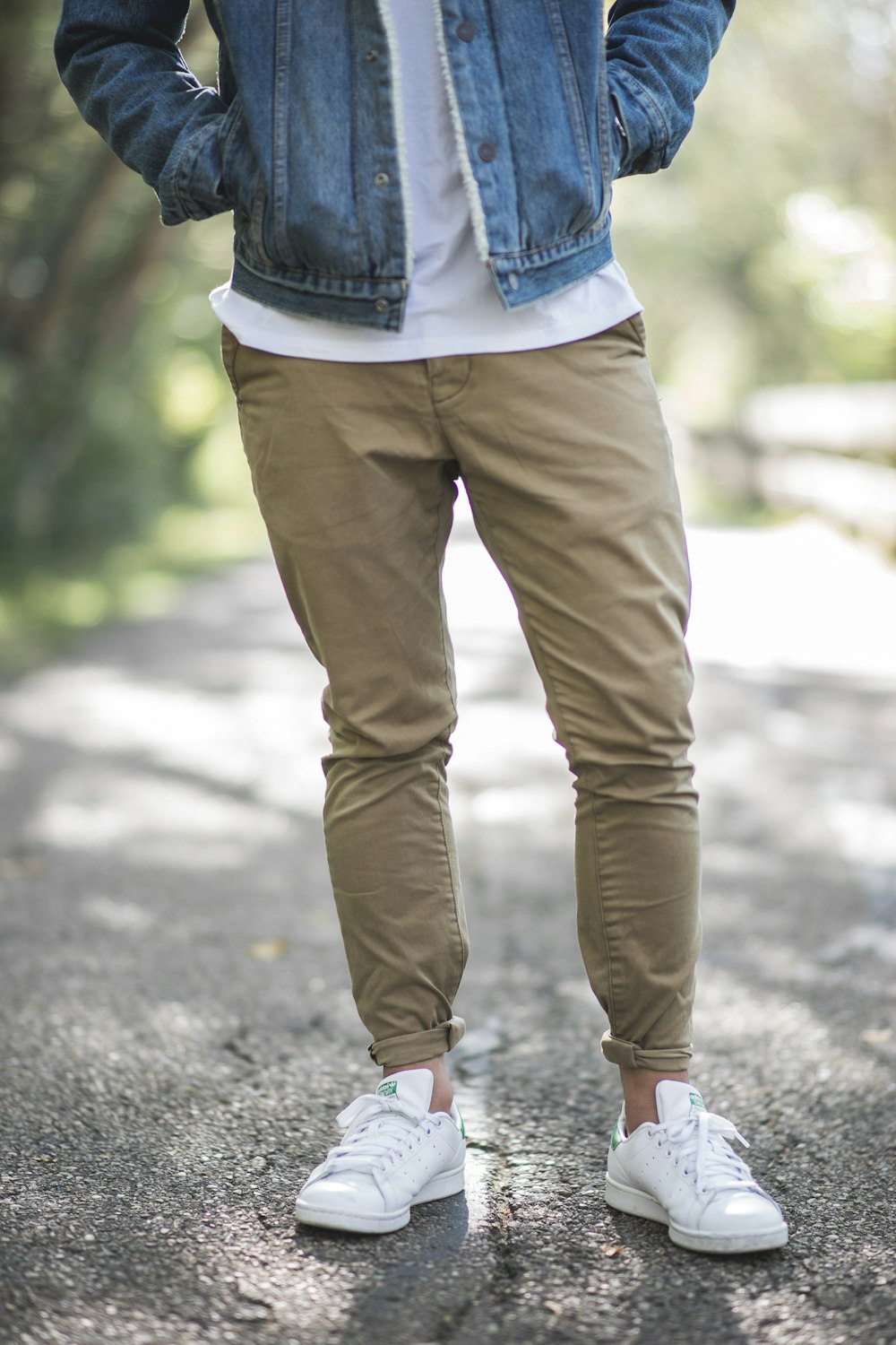 Hombre con jeans ajustados marrones y zapatillas de deporte parado en la carretera durante el día