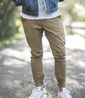 man wearing brown fitted jeans and sneakers standing on road at daytime