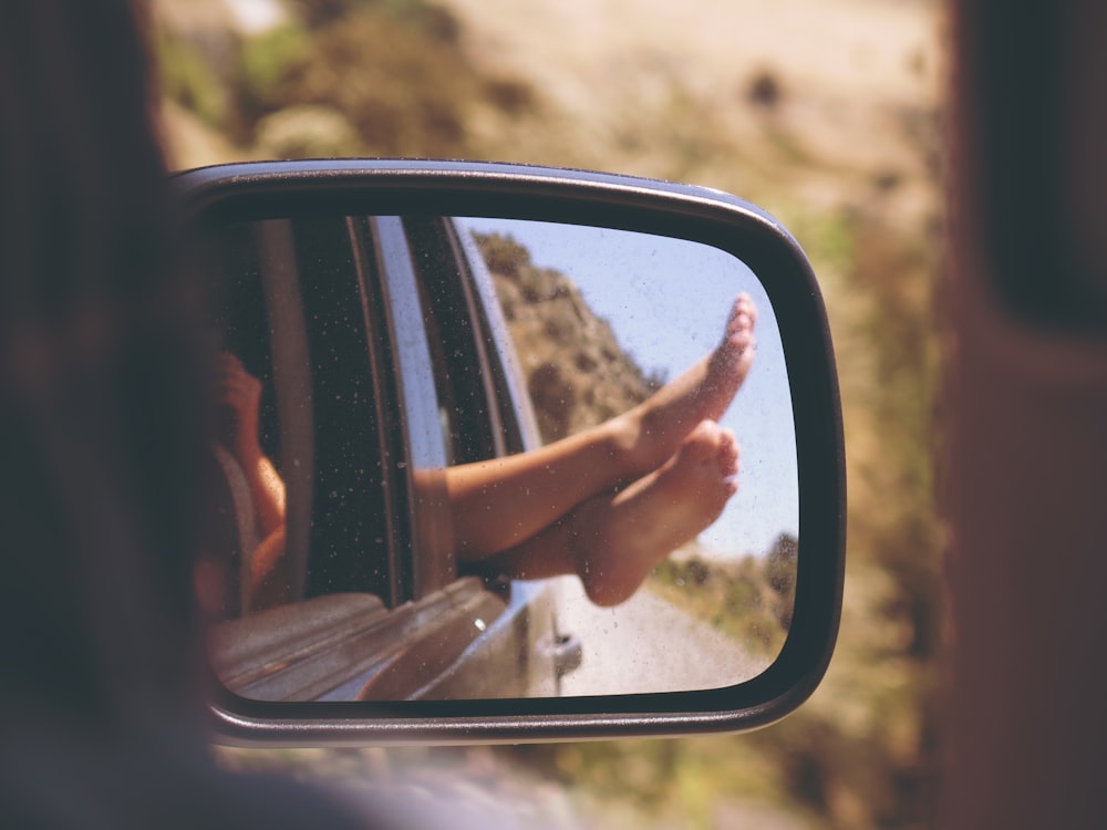 A person sticking their feet out of a car window from the perspective of the rear view mirror