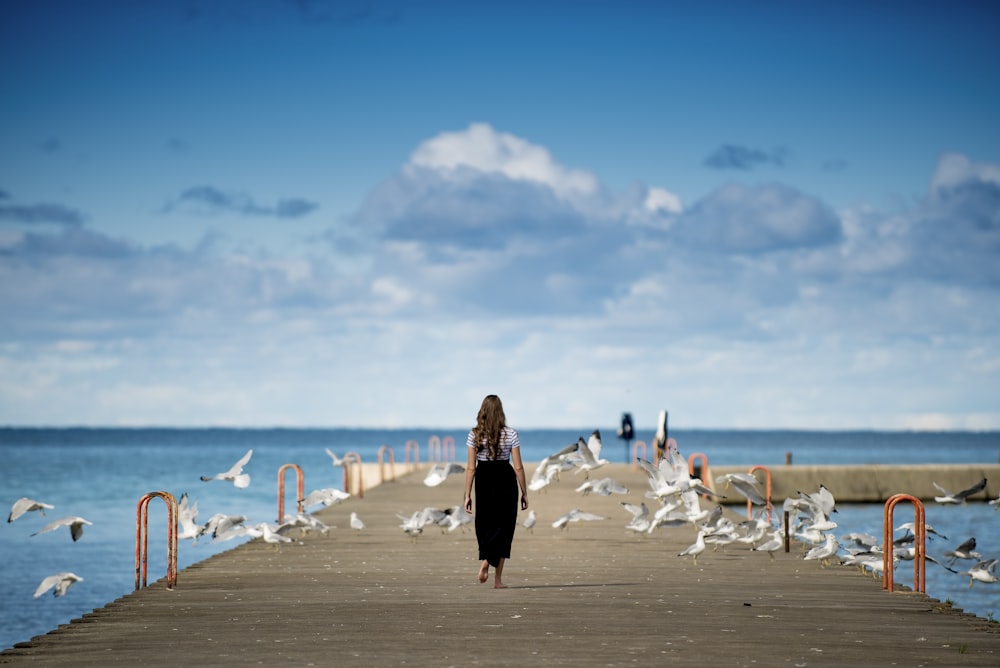 woman standing on a boardwalk surrounded by birds