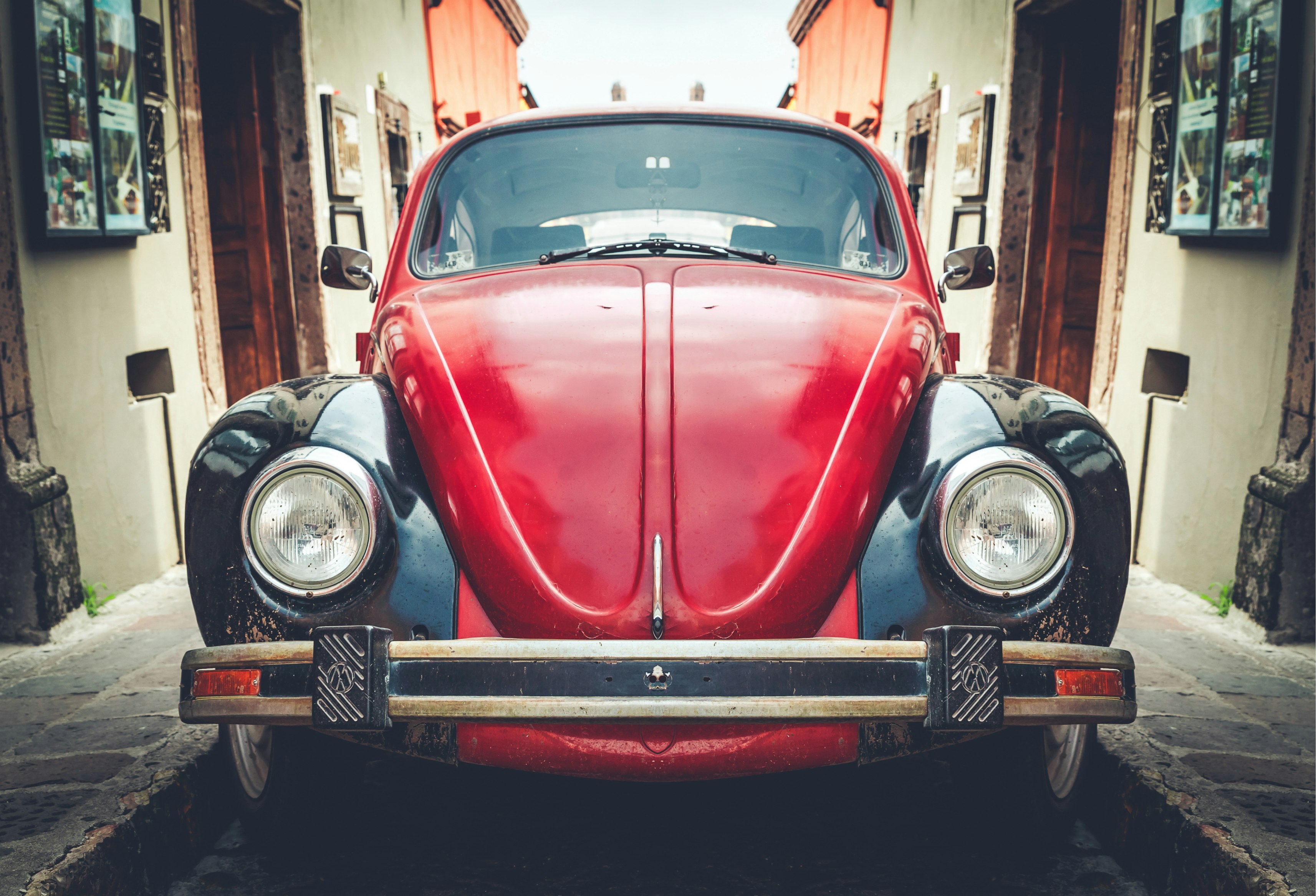 photo of red and black Volkswagen Beetle in alley