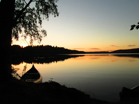 A serene lakeshore at sunset with soft outdoor lights illuminating a canoe resting by the water.