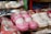 Brightly colored children's shoes are displayed closely together. The shoes are made of glossy materials and come in shades of pink and white. Some of the shoes feature decorative accents such as floral designs and small bows.