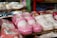 Brightly colored children's shoes are displayed closely together. The shoes are made of glossy materials and come in shades of pink and white. Some of the shoes feature decorative accents such as floral designs and small bows.