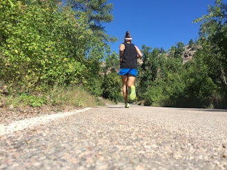 Athlete running on a trail surrounded by lush green forest under a clear sky