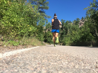 Runners traversing a forest trail surrounded by lush green trees under a clear blue sky.