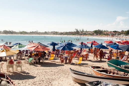 A vibrant beach scene with colorful umbrellas, coolers, and people enjoying a sunny summer day.