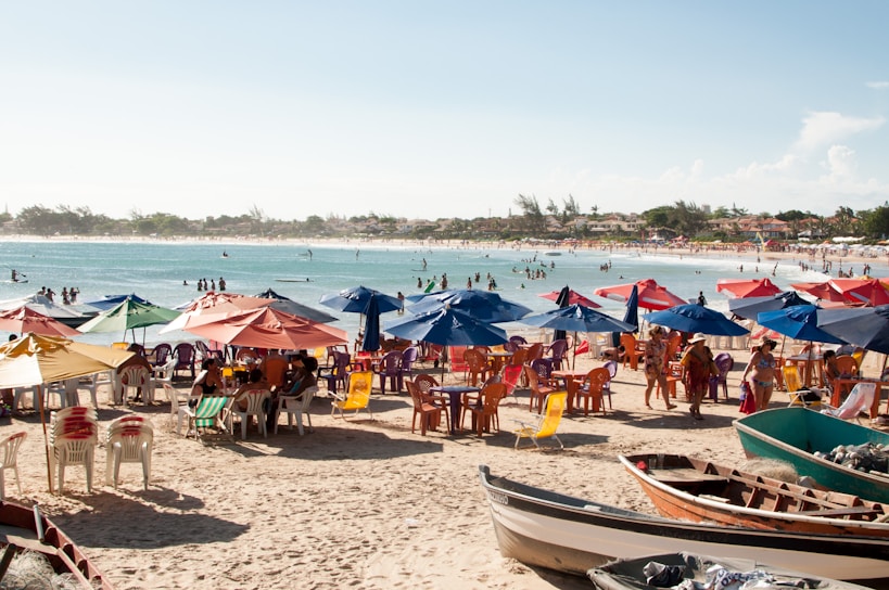 A vibrant beach scene with colorful umbrellas, coolers, and people enjoying summer sun.