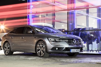 A sleek metallic grey car parked outside the cs-mobil dealership in Bavaria under a bold red sky at dusk.