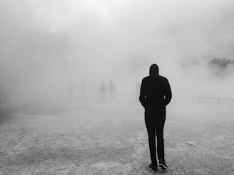 Moody, grainy close-up of a shadowy masked figure emerging from dense fog.