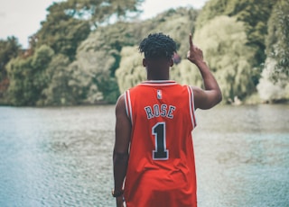 man standing facing body of water while raising his right arm