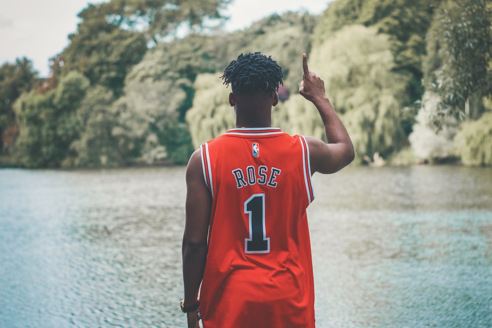 man standing facing body of water while raising his right arm